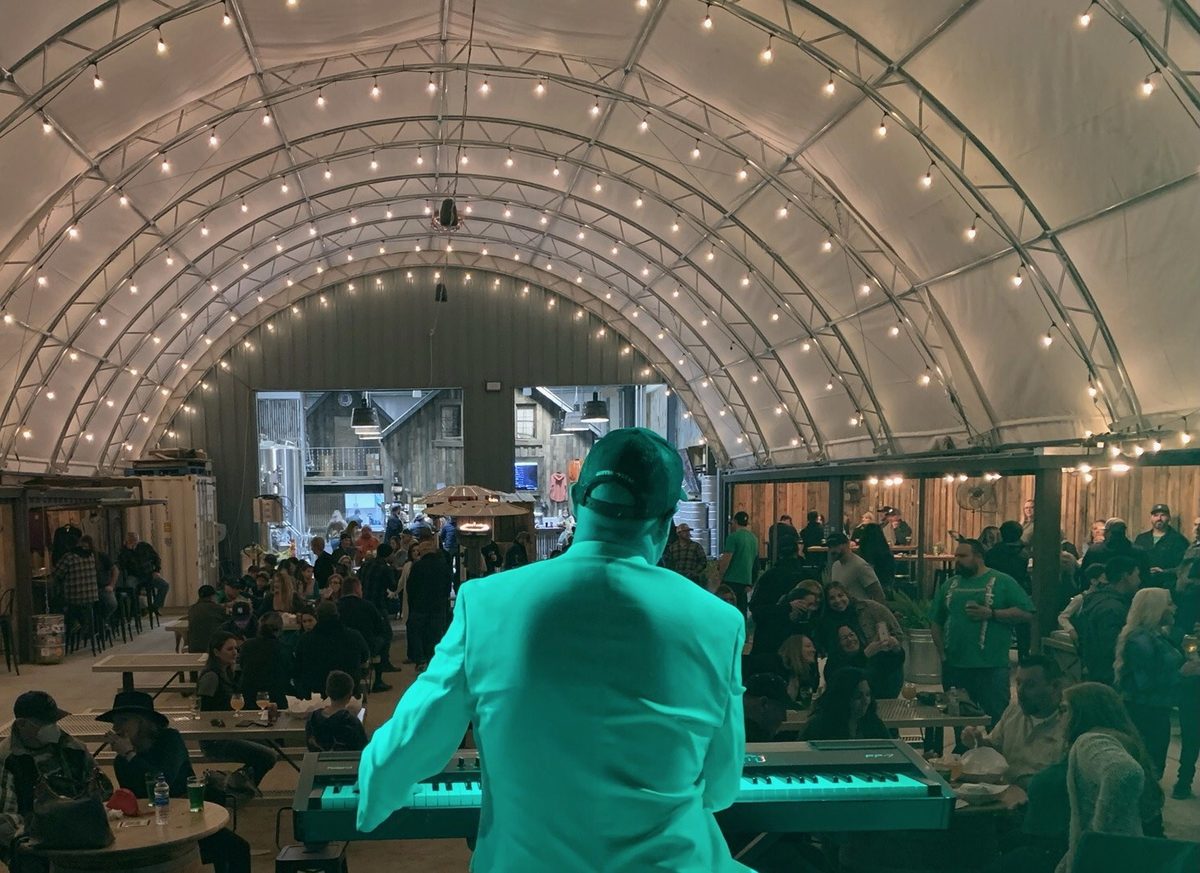 A dueling piano player at the keys looking out at a full room under string lights